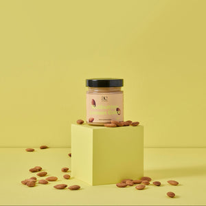 Glas Nutbutter Lemon Cake von ae kitchen auf gelbem Podest, umgeben von Mandeln, vor gelbem Hintergrund