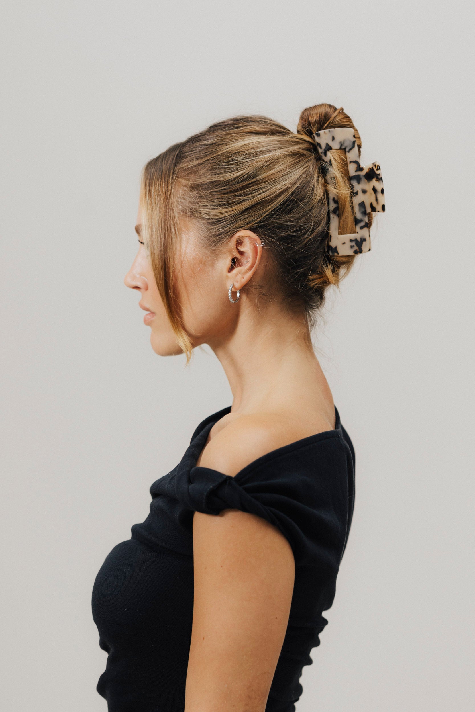 Frau mit hochgestecktem Haar, gehalten von einer großen Haarklammer im Tortoise-Look. Sie trägt ein schwarzes Off-Shoulder-Oberteil und silberne Creolen.
